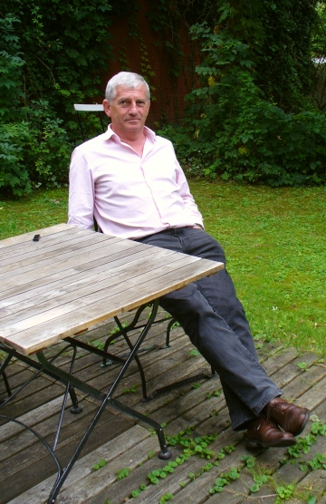 Arnold Stadler sitzt auf Gartenstuhl in seinem Garten in Sallahn im Wendland und hat damit einen Ort jenseits der Konferenzbestuhlung gefunden