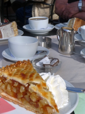 Auf dem Tisch einer Caféterasse ist ein Stück Apfelkuchen mit Sahne zu sehen. Aber auch eine Tasse auf der Terrasse. Foto von Georg Magirius